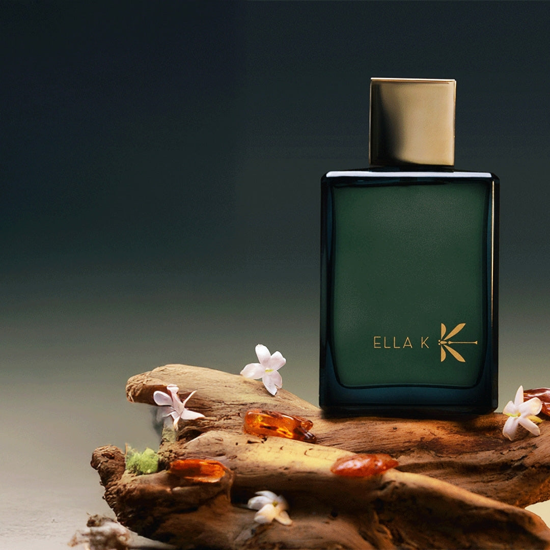 Eleganter Parfumflakon von Ella K „Myrrh K“ mit goldener Kappe auf Treibholz arrangiert, umgeben von Myrrheharz und zarten weißen Blüten vor dunklem, stimmungsvollem Hintergrund