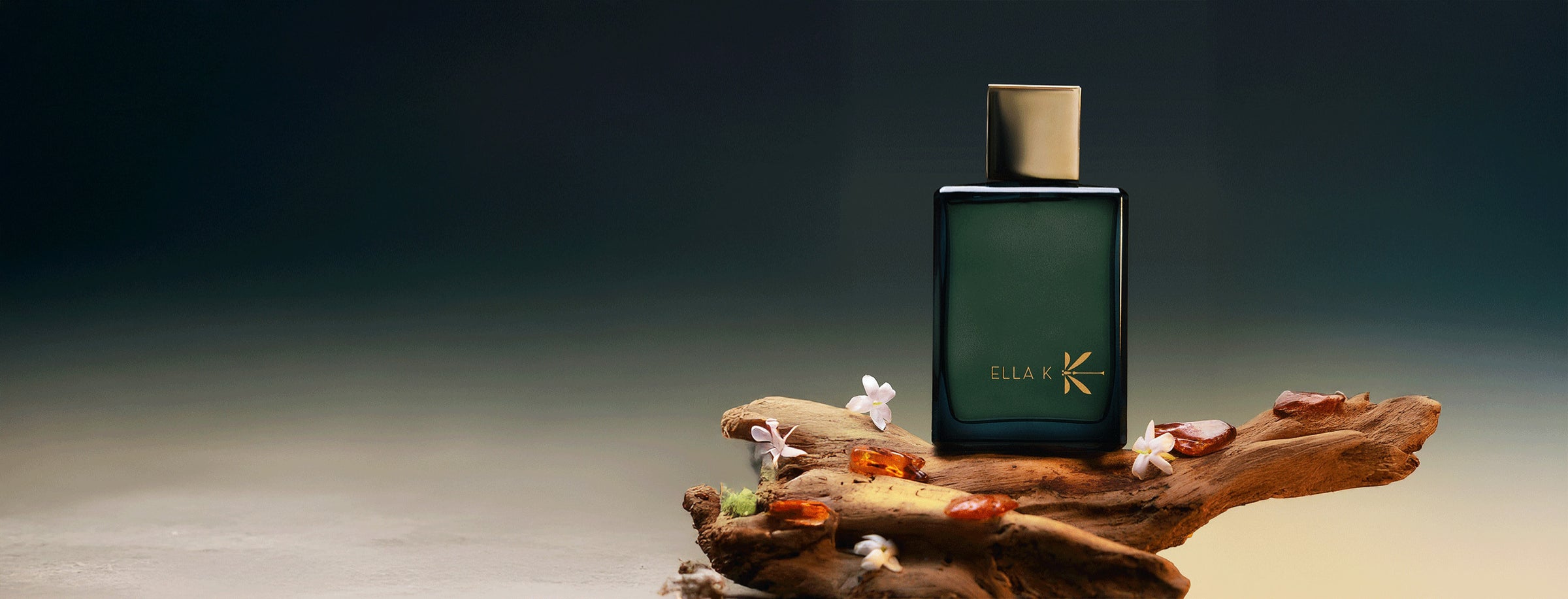 Eleganter Parfumflakon von Ella K „Myrrh K“ mit goldener Kappe auf Treibholz arrangiert, umgeben von Myrrheharz und zarten weißen Blüten vor dunklem, stimmungsvollem Hintergrund